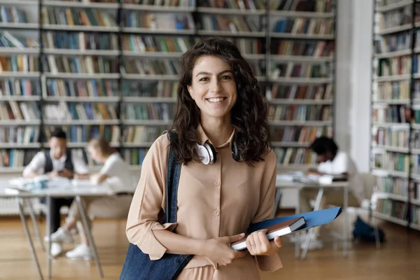 Glad latinamerikansk gen Z student flicka med hörlurar besöker biblioteket — Stockfoto