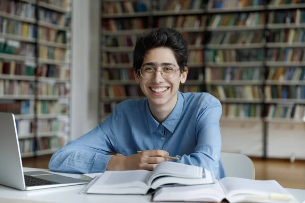Feliz estudiante fresco en gafas redacción ensayo en la biblioteca —  Fotos de Stock