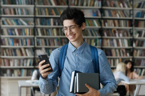 Eccitato giovane studente ragazzo in occhiali in possesso di libri accatastati — Foto Stock