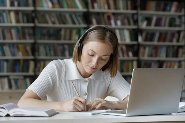Studentessa seria ascoltando tutorial audio da cuffie wireless, — Foto Stock