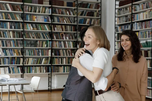 Счастливые молодые студенты университетов обнимаются в библиотеке — стоковое фото