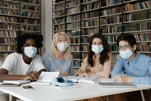 Multiethnic team of students in masks sitting at table — Stock Photo, Image