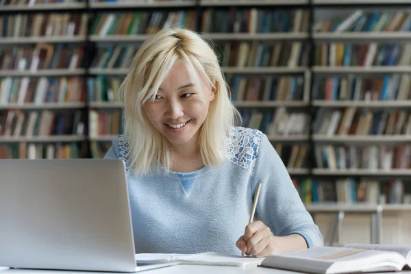 Felice asiatico studente ragazza fare compiti in college biblioteca — Foto Stock
