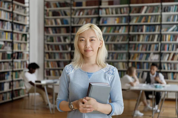 ความมั่นใจ บวก เอเชีย สาวผมบลอนด์วิทยาลัย ยืนอยู่ในห้องสมุดมหาวิทยาลัย — ภาพถ่ายสต็อก