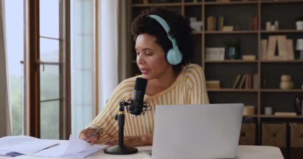 Afrikansk kvinna i hörlurar pratar i mikrofon och skriver anteckningar — Stockvideo