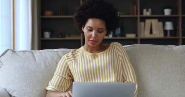 Африканская женщина сидит на диване с ноутбуком участвует в видеоконференции — стоковое видео