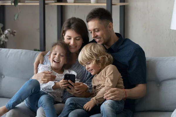 Lachende jonge ouders spelen mobiele games met kleine kinderen. — Stockfoto