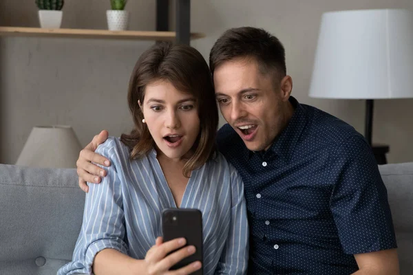 Verrast gelukkig jong familie paar op zoek naar smartphone scherm. — Stockfoto