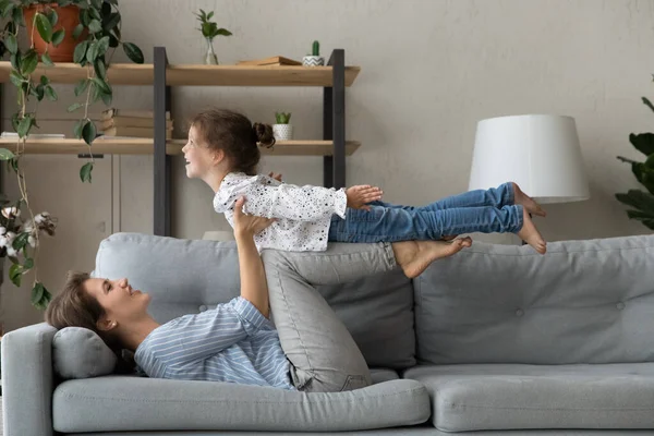 Alegre madre milenaria levantando en el aire riendo hija. — Foto de Stock