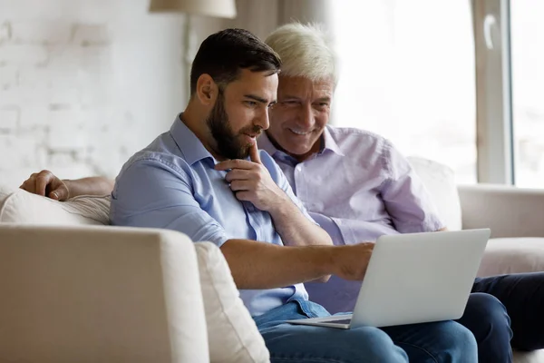 Feliz hijo adulto enseñando a papá mayor a usar la aplicación de Internet — Foto de Stock