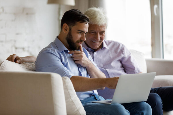 Happy grownup son teaching senior dad to use internet application