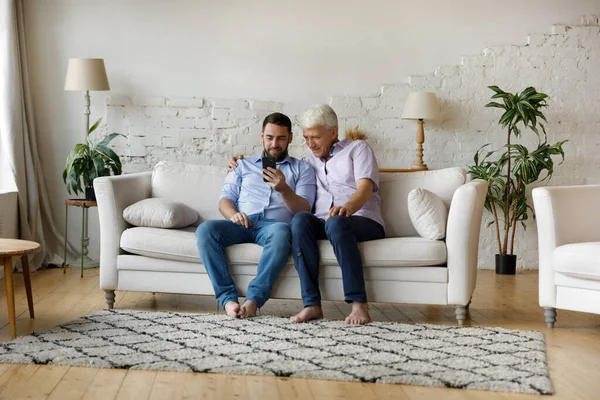 Feliz padre de pelo gris maduro e hijo adulto compartiendo teléfono inteligente — Foto de Stock