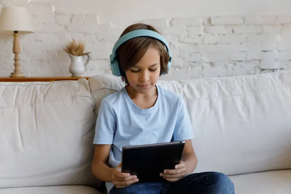 Serieuze gefocuste schoolkind jongen in draadloze koptelefoon lezen boek — Stockfoto