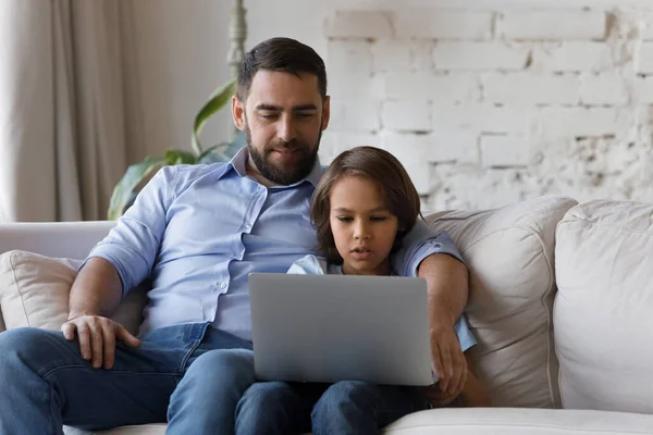 Glad pappa tittar på fokuserad skolunge son med hjälp av lärande online app — Stockfoto