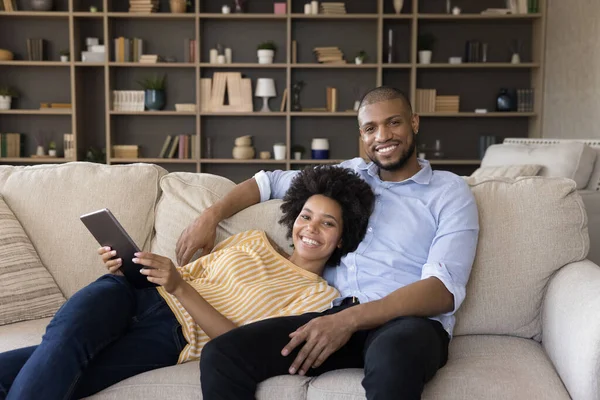 Afrikanisches Paar hält Tablet entspannt auf Sofa und blickt in Kamera — Stockfoto