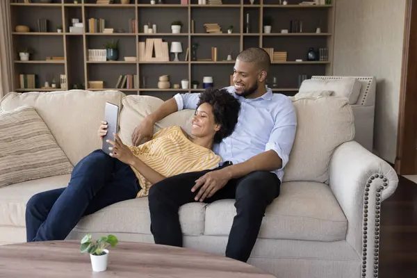 Africano cônjuges relaxante no sofá na sala de estar usando tablet — Fotografia de Stock