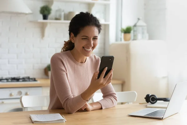 Žena sedět uvnitř drží moderní smartphone směje se na online video — Stock fotografie