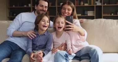 Çocuklu bir aile kanepeye oturup cep telefonuyla eğleniyor.