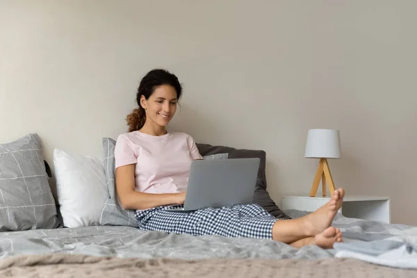 Ontspannen vrouw in pyjama zitten op bed met laptop — Stockfoto