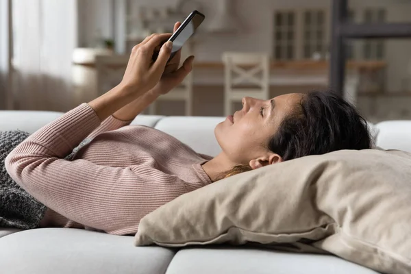 Serene vrouw ontspannen liggend op kussen op de bank met smartphone — Stockfoto