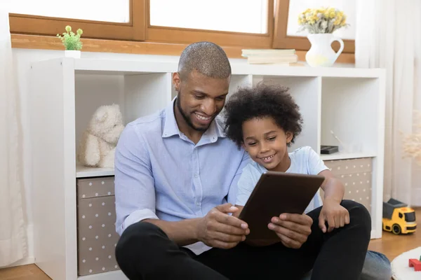 Africano padre su pequeño hijo tener divertido uso digital tablet —  Fotos de Stock