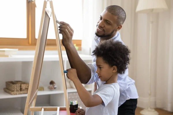 Afrikaanse vader en zoontje tekenen op schoolbord met krijtjes — Stockfoto