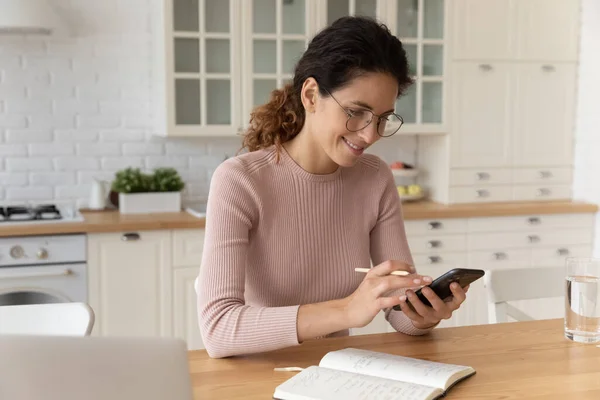 Mujer sosteniendo teléfono inteligente y lápiz, comprobar el horario de planificación de la casa — Foto de Stock