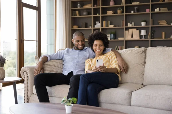 Feliz pareja africana sentarse en el sofá con el teléfono celular —  Fotos de Stock