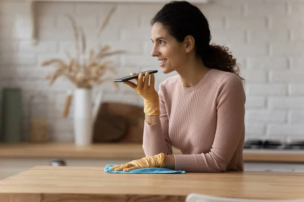 La ama de casa latina mantiene conversaciones de teléfonos inteligentes en el altavoz mientras limpia la cocina — Foto de Stock