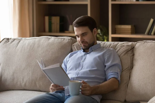 Sorrindo relaxado jovem envolvido na leitura de livro de papel. — Fotografia de Stock