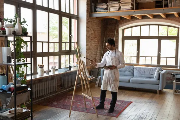 Junger männlicher Künstler, der im heimischen Atelier an der Staffelei steht — Stockfoto