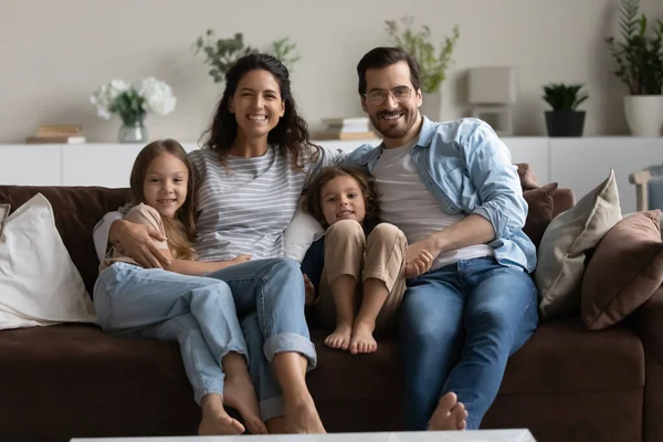 Paar en kinderen zitten op de bank glimlachend naar de camera te kijken — Stockfoto