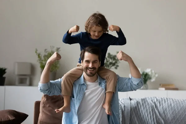 Kleiner Sohn sitzt auf der Schulter des Vaters und demonstriert Bizepsstärke — Stockfoto