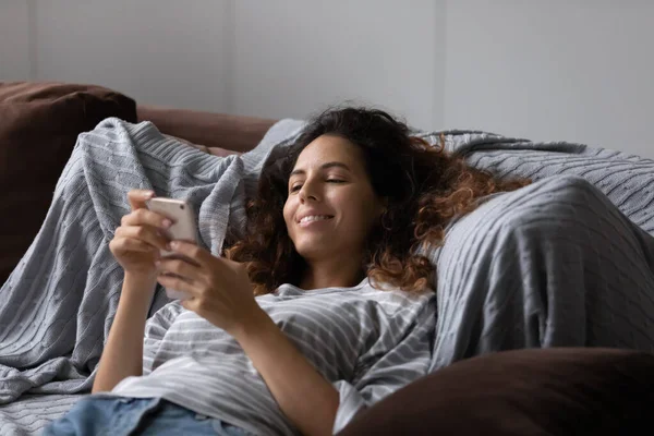 Mladá atraktivní hispánská žena odpočívající na pohovce s chytrým telefonem — Stock fotografie