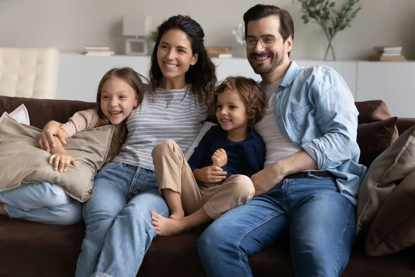 Семья сидит на диване дома улыбаясь глядя вдаль — стоковое фото