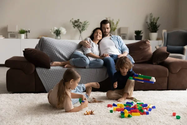 Couple se détendre sur le canapé leurs enfants jouent avec des briques colorées — Photo