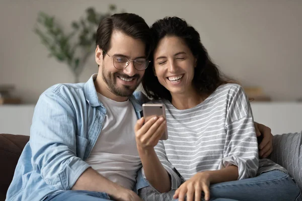 Genç ve gülen bir çift akıllı telefonlarıyla kanepede oturuyor. — Stok fotoğraf