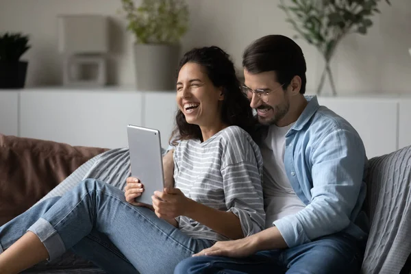 Χαρούμενο ζευγάρι που γελάει κάθεται στον καναπέ με ψηφιακό tablet — Φωτογραφία Αρχείου
