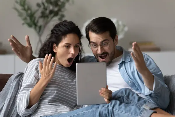 Förbluffade par gawp på digital tablett känner sig förvånad över nyheter — Stockfoto