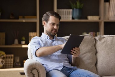 Rahat gülümseyen genç adam dijital dokunmatik cihaz kullanıyor..