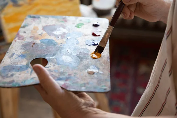 Художник держит прямоугольную палитру, используя кисть, смешивая краски — стоковое фото
