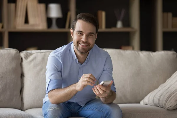 Ritratto di giovane uomo sorridente e rilassato che usa il cellulare a casa. — Foto Stock