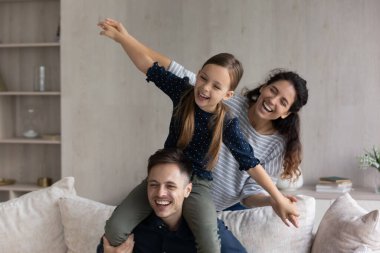 Gülen kız babasının omuzlarında oturuyor, aile komik oyunlar oynuyor.
