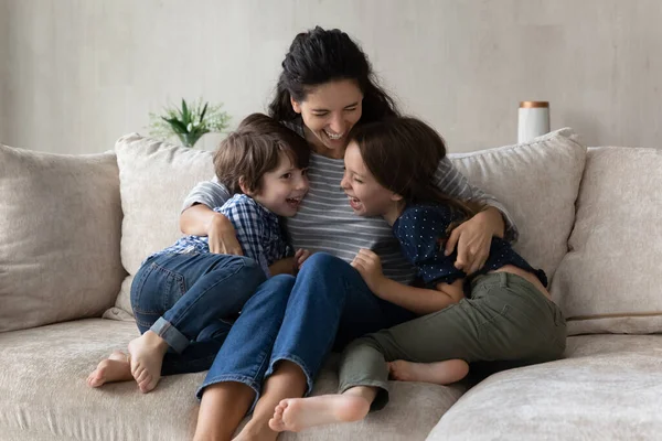 Lachende Mutter umarmt Sohn und Tochter, sitzt auf Couch — Stockfoto