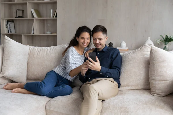 Счастливая пара с помощью смартфона, расслабляясь на диване вместе — стоковое фото