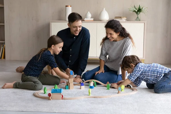 Glückliche Eltern und zwei Kinder spielen mit Holzeisenbahn — Stockfoto