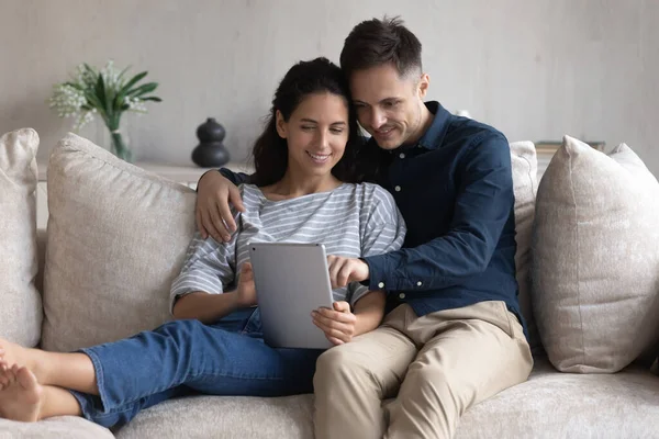Улыбающаяся молодая пара с помощью планшета вместе, сидя на диване — стоковое фото