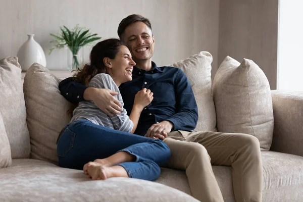 Laughing couple hugging, relaxing sitting on couch together — Stock Photo, Image