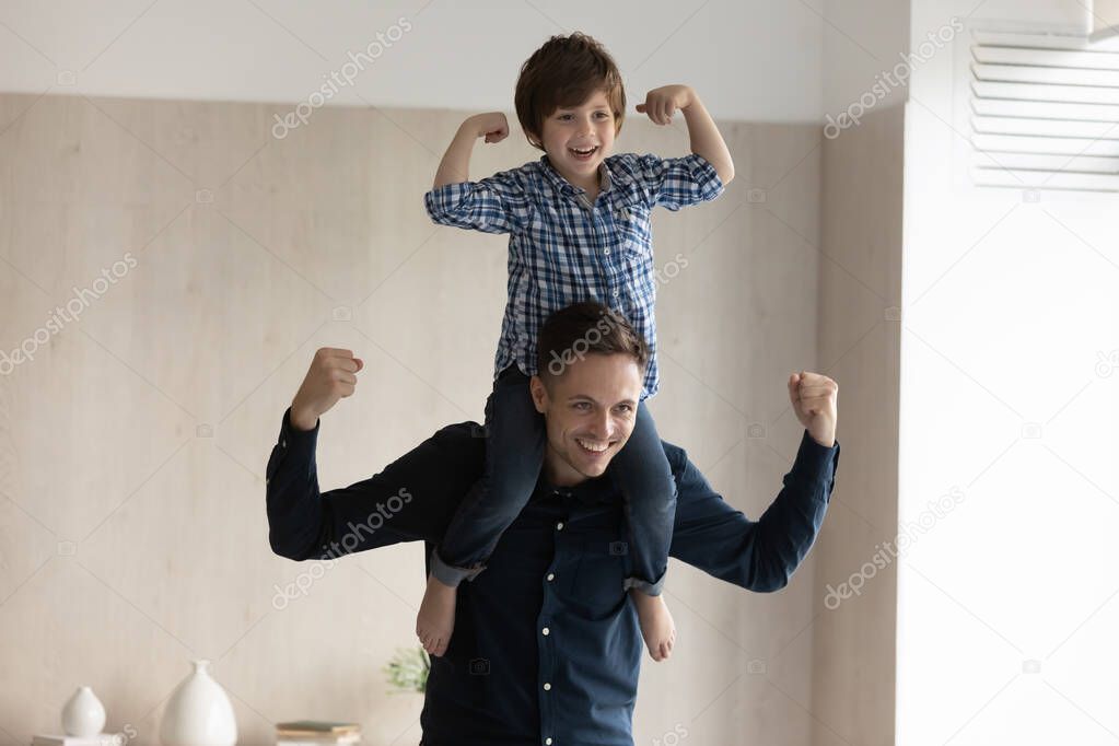 Happy little son sitting on father shoulder, showing strength