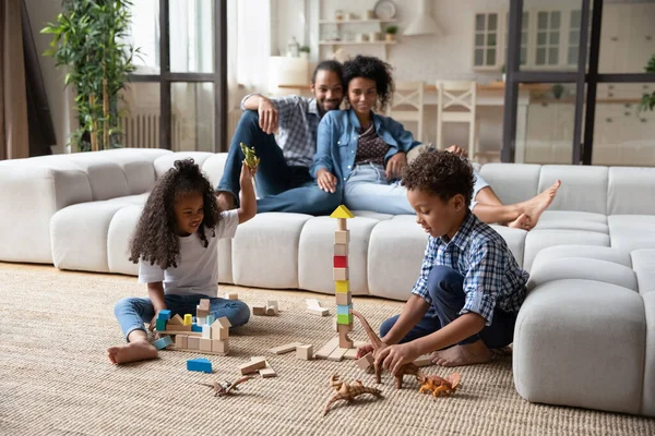 Gelukkig Afrikaanse ouders kijken naar kleine kinderen spelen speelgoed. — Stockfoto